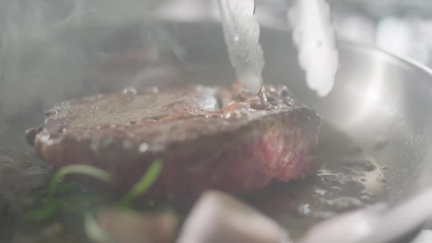 Steak cooking in a frying pan is flipped over