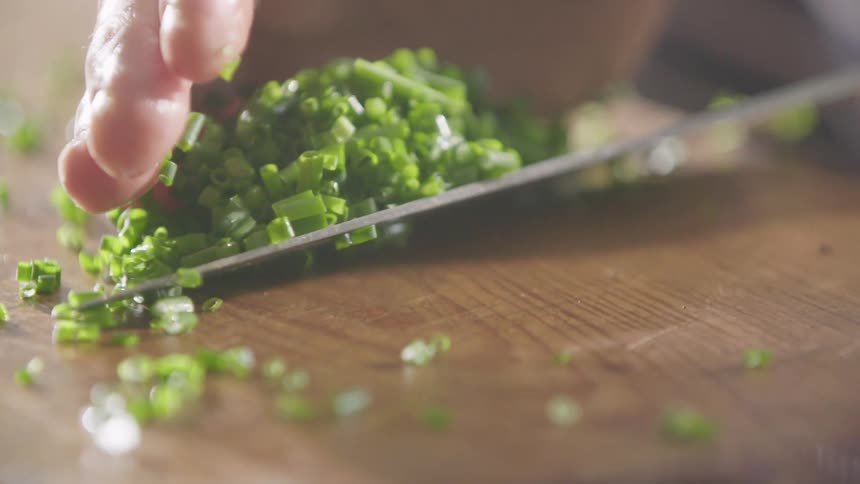 A white male uses his hand a knife to scoop up some cut greens