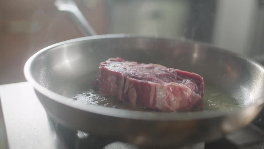 A person is cooking a steak on the pan