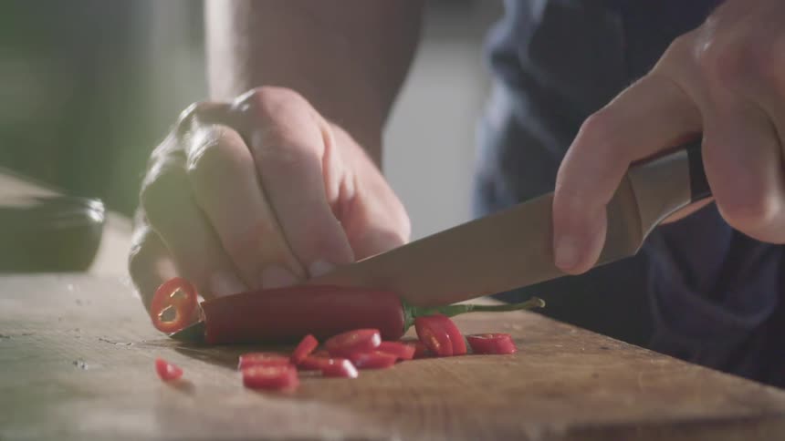 A person uses a knife to cut a red pepper on a cutting board