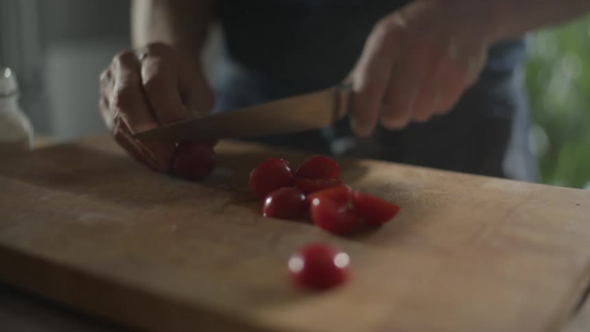 Small tomatoes being sliced on a wood cutting board