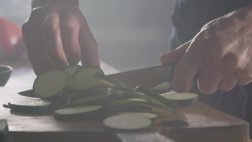 Cook slices a cucumber with a knife on a cutting board in the kitchen