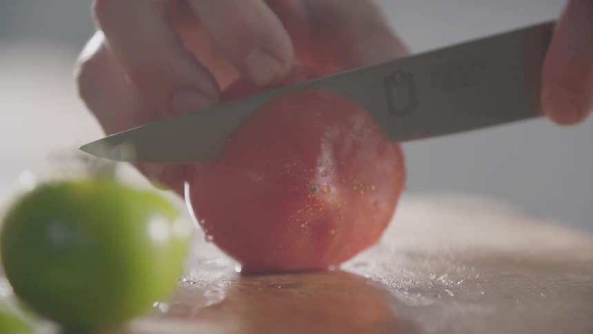 Cook cuts a tomato with a sharp knife on a cutting board in the kitchen