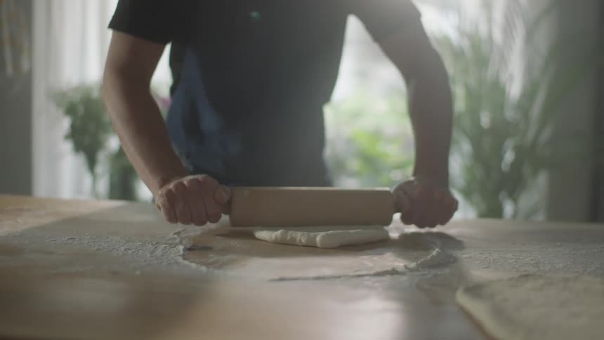 Man uses rolling pin to flatten dough over a floured table in the kitchen