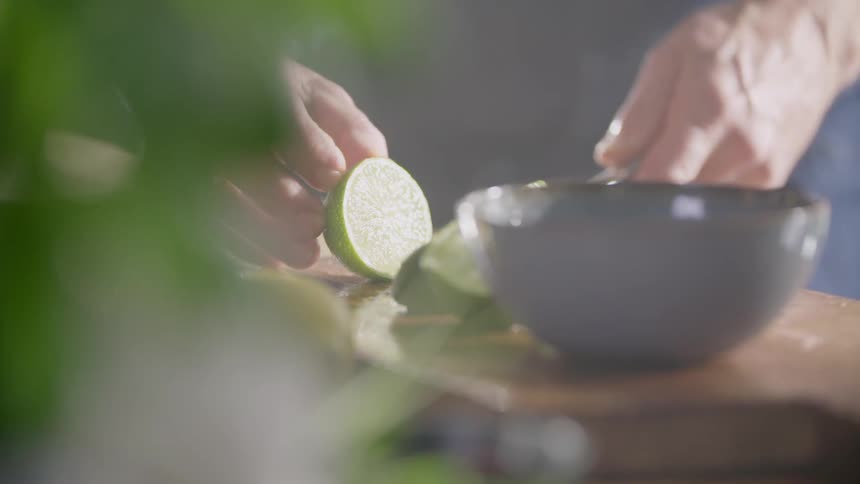Man cuts a lime in half with a sharp knife on a cutting board in the kitchen