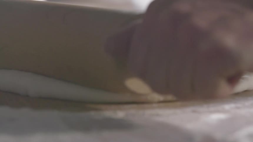 A white male uses a rolling pin to flatten a piece of dough