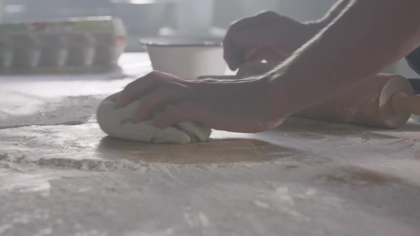 Man kneads dough on a floured table in the kitchen