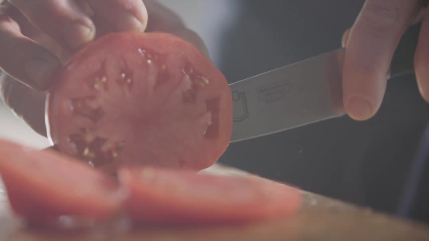 Slices of tomato being sliced with a chef knife