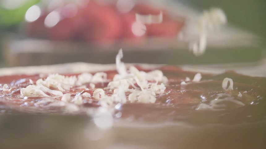 White shredded cheese is spread across tomato sauce covered pizza crust