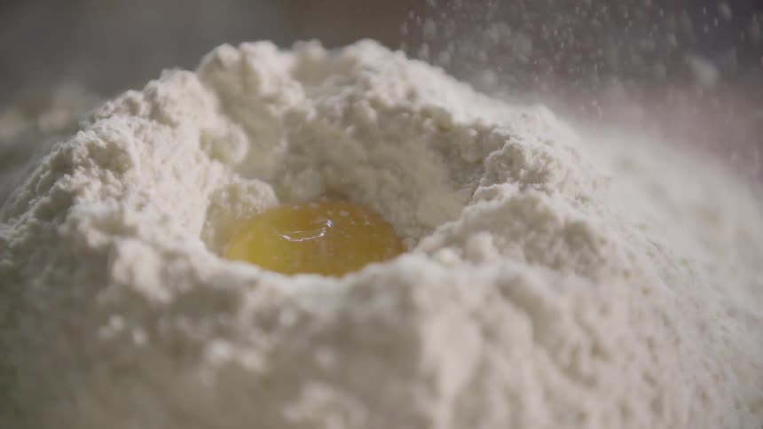 A pile of flour with an egg yolk falling into it