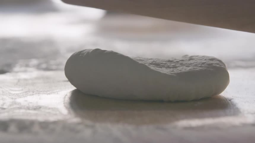 Man rolls out pizza dough with a rolling ping in the kitchen