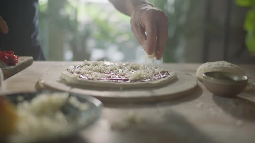 Hand picking up shredded cheese then sprinkling on top of a pizza