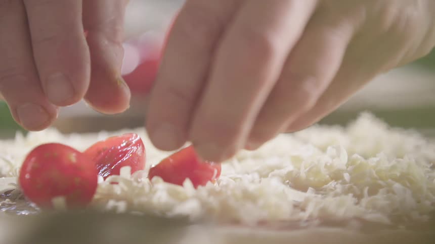 A person places tomatoes on the pizza