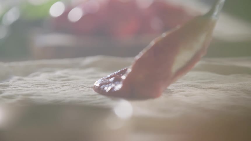 Spoon spreading sauce across pizza dough