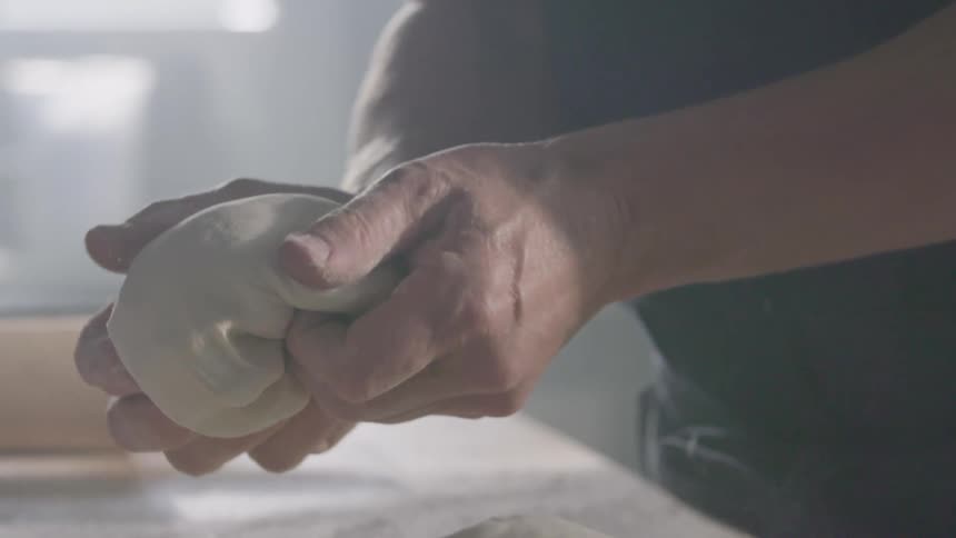 Man with a black shirt kneads dough in the kitchen