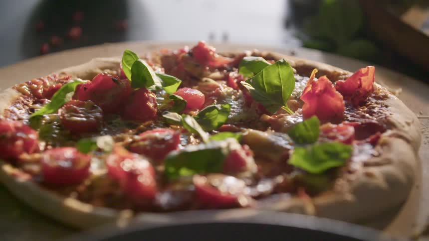 Hand adding fresh basil leaves on a personal pizza