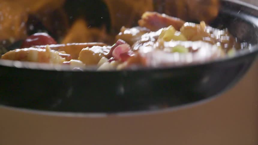 A pan of shrimp and vegetables is mixed and flambed over a stove