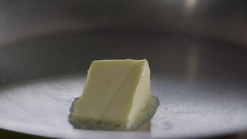 Hand placing slice of butter on hot pan to melt