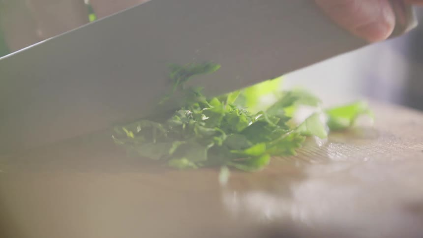 Man chops parsley with a sharp knife on a cutting board in the kitchen