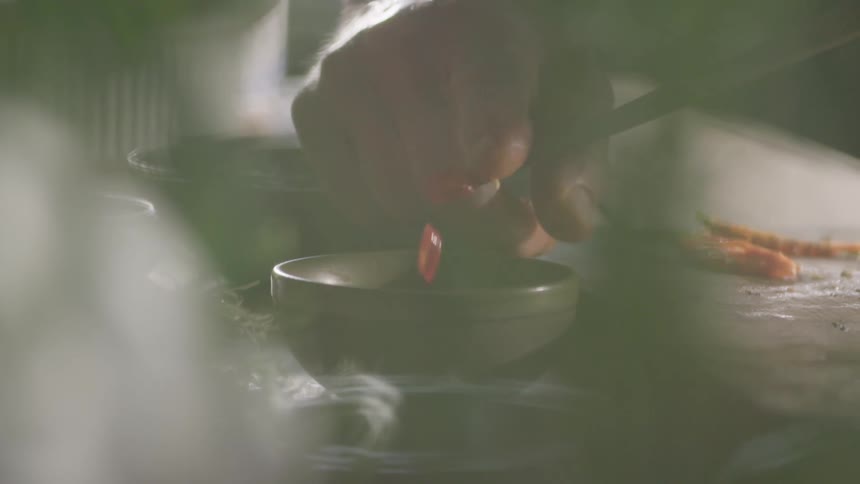 A man slides sliced chili peppers off a knife and into a small bowl