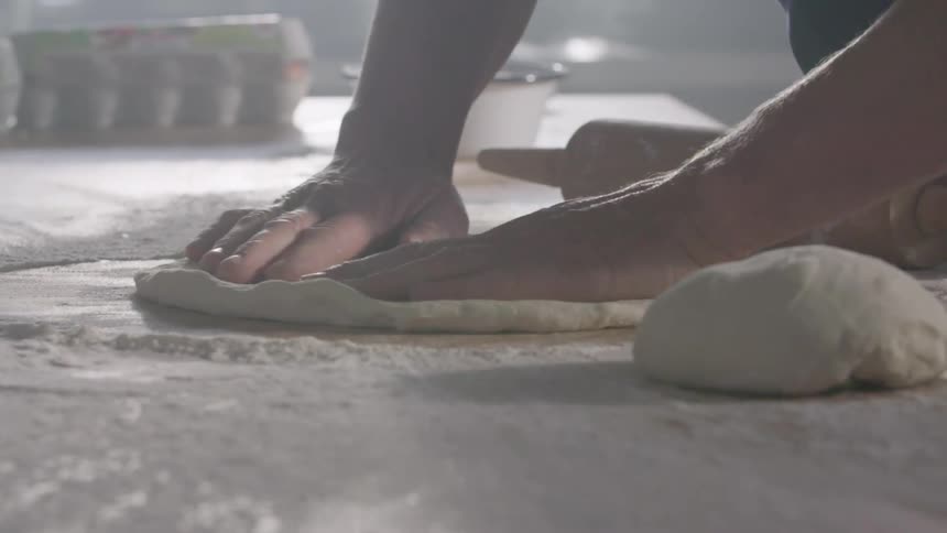 A man stretches and shapes pizza dough on a floured surface
