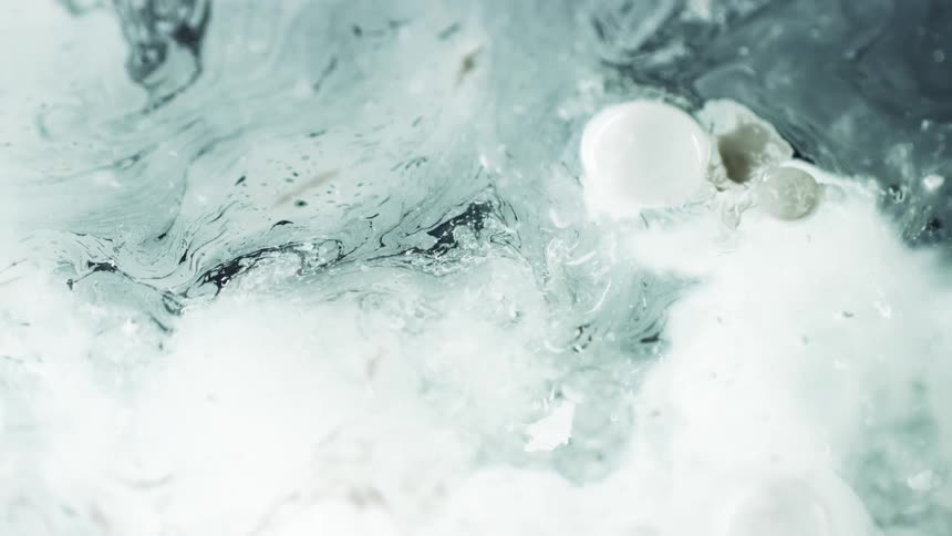 Thin white paint is thrown into gray liquid floating and bubbling on the surface