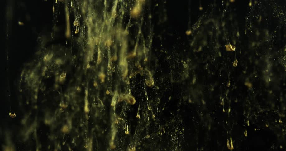 Yellow gold dye drips down in a vat of liquid