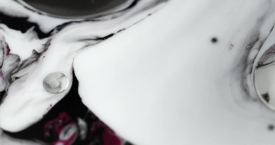 Black ink with red spots swirl on the surface of a white liquid