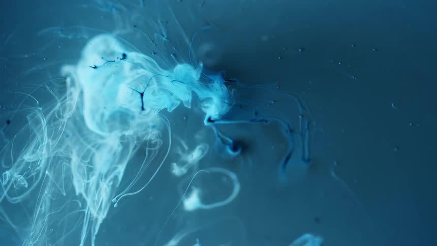Blue dye drops and blends into liquid as white tendril flow