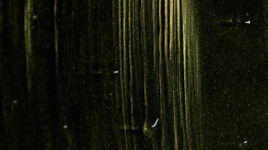 Lines of gold glitter slowly drip down a pane of clear glass