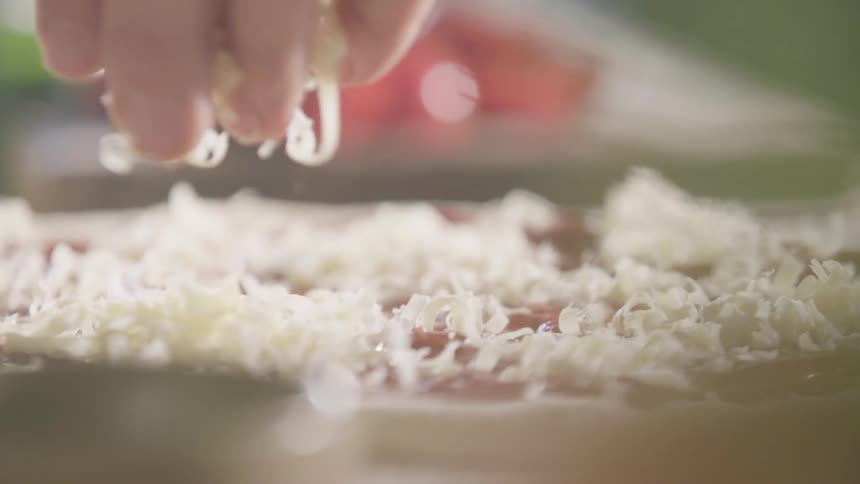 Someone is spreading cheese on a pizza