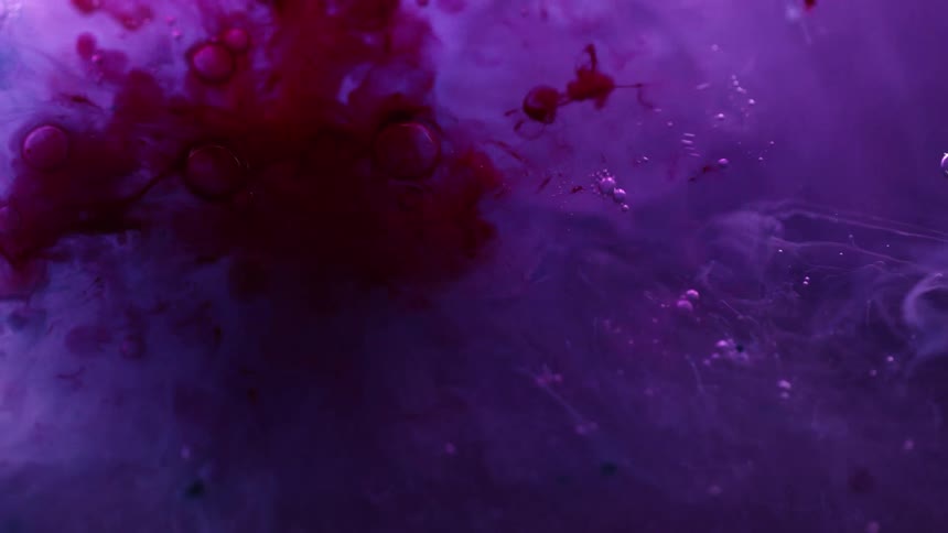 Red ink drips into purple liquid and spreads