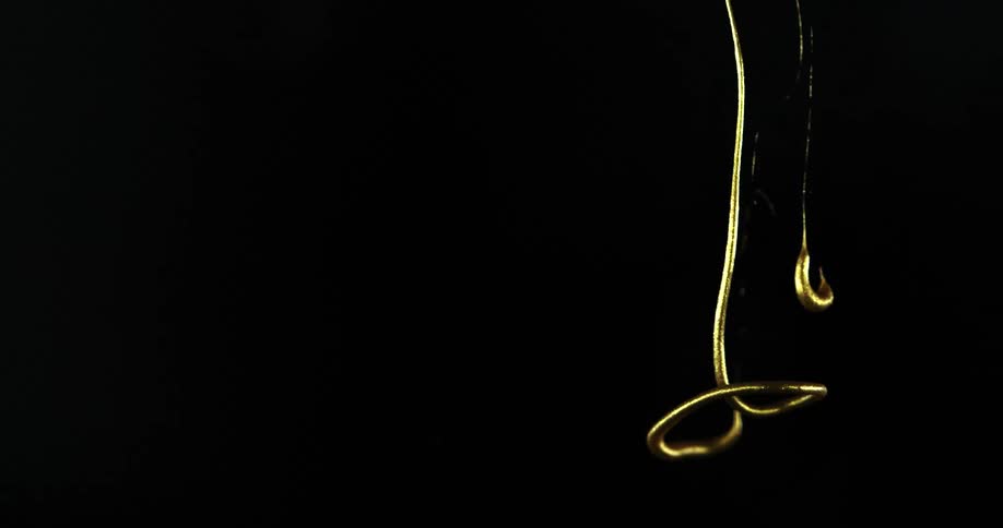 String of gold ink swirls down water against a black background