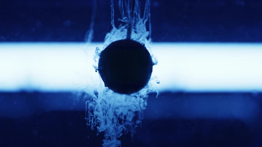Ink sinking on a backlight water tank swirls around a ball suspended in the middle