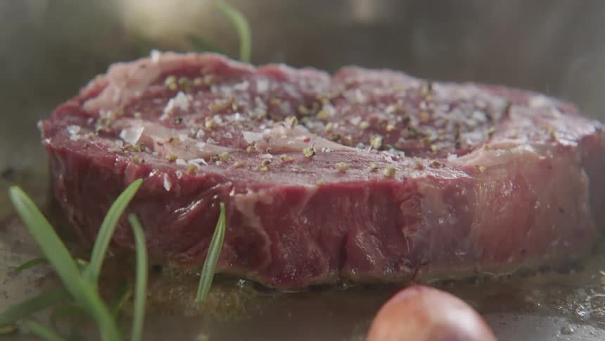 A man puts herbs in a pan as he cooks meat