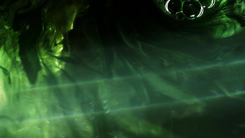 Green shimmering ink floating in a tank full of water