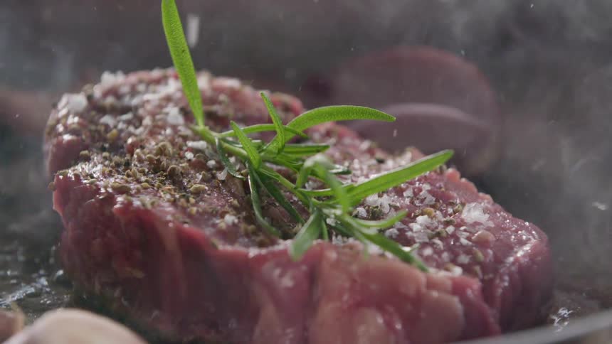 Salt falling on a piece of meat as it cooks in a pan
