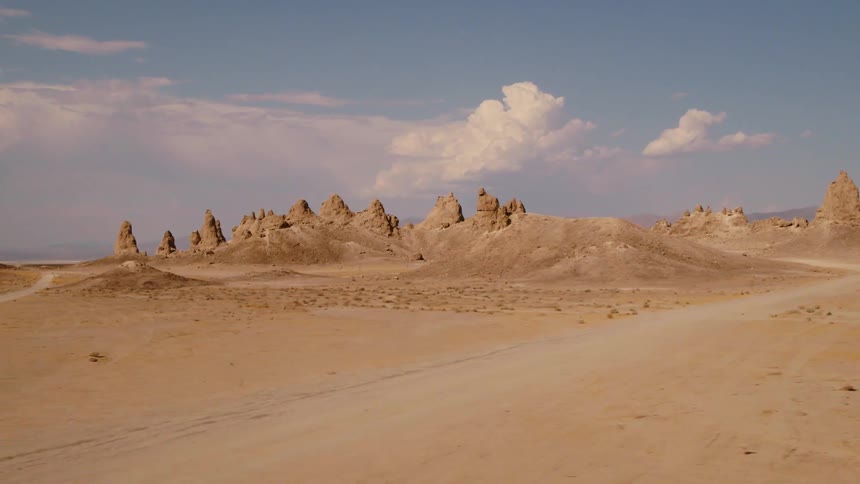 A dirt road running through a desert spotted with rock formations jutting into the sky