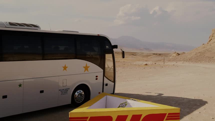 Charter bus on dirt road through vast desert landscape