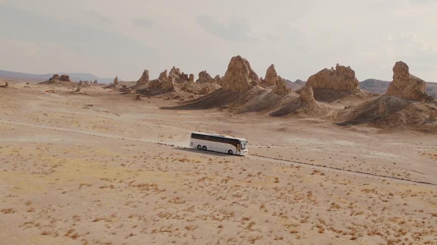 Aerial view of a white bus driving down a dirt road in desert