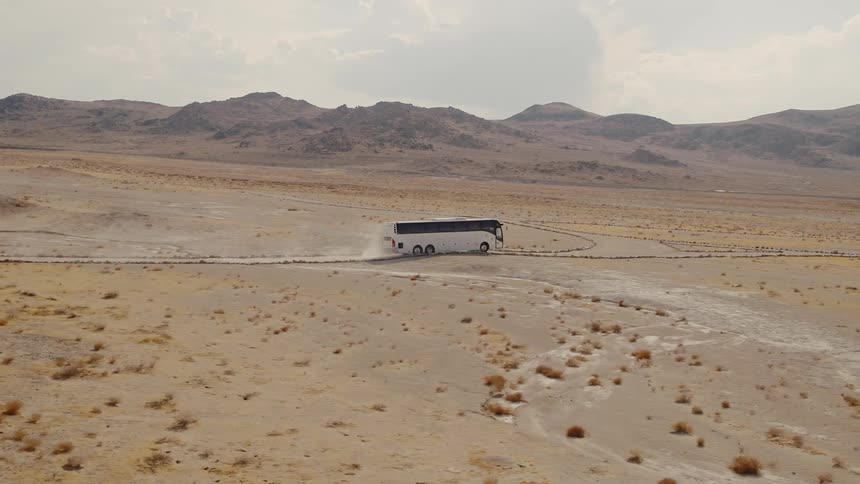 Aerial view of a white bus driving on a dirt road in desert