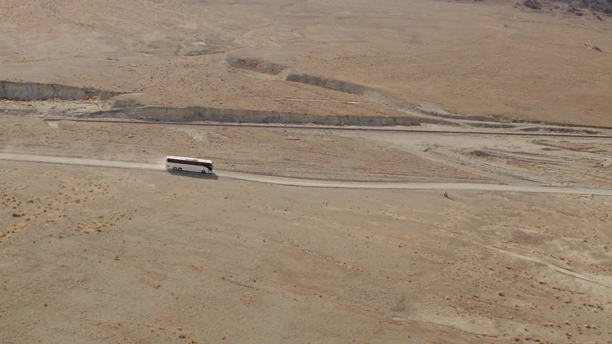 White bus travels on a dirt road in the desert