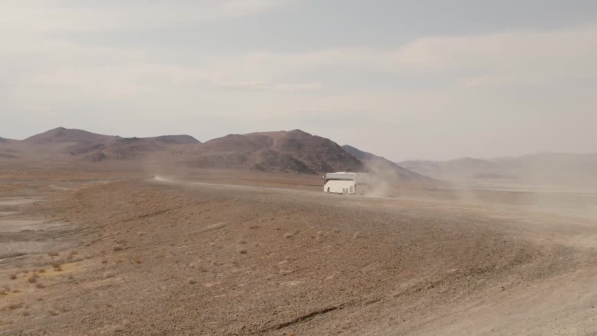 A white bus drives down a dirt road in the desert