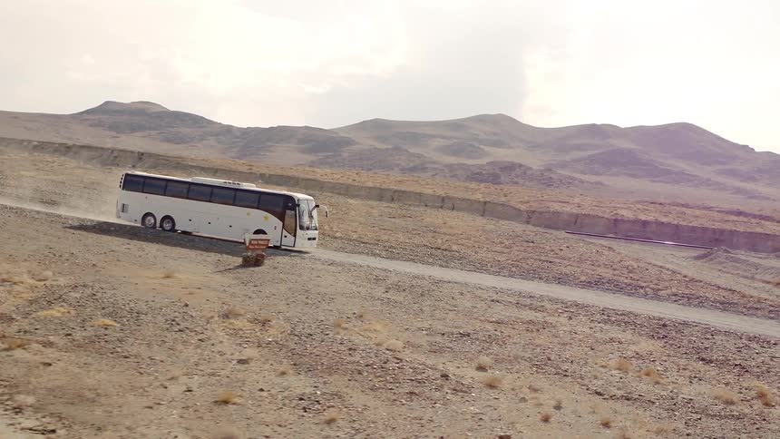 Aerial view of a white bus drives down a dirt road in desert