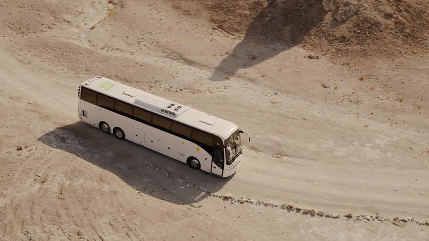 Tour bus drives on a dirt road through the desert