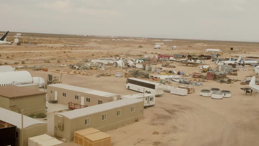 Aerial of a bus driving through an airplane graveyard in the desert