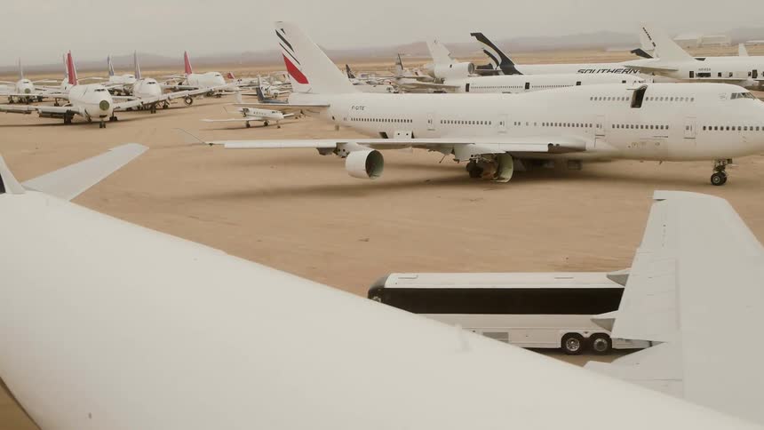 A bus travels through a vast dirt field filled with large aircraft