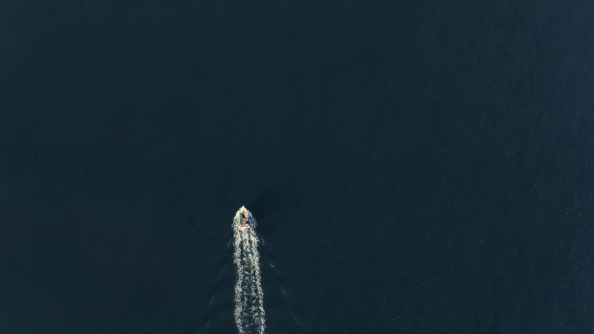 Boat cuts through dark blue water leaving wake