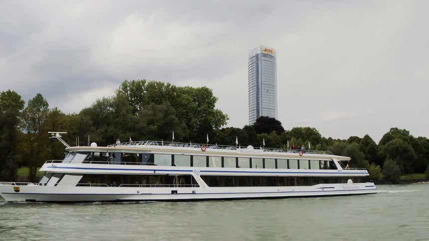 A yacht on a river with trees and a skyscraper in the background