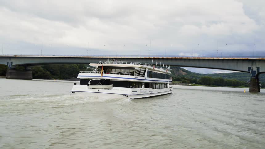 A white ferry boat travels across a river to pass under a bridge on a cloudy day